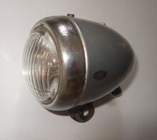 Scheinwerfer Typ 8707.5/3 Zeitraum: 1956 bis 1958 Verwendung: vrmtl. Zubehörteil Material: Stahlblech, Glas Ø Lichtaustritt: Farben/Varianten: silber Bemerkungen: Oberseite geprägt mit Gütezeichen "S" und Betriebsnummer, Typen-Nummer und Herstellungsjahr seitlich unten geprägt