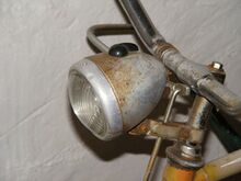 Scheinwerfer Typ SF 13/3 Zeitraum: 195x bis vrmtl. 1957 Verwendung: Mifa Fahrräder, Simson Tourensporträder Material: Stahlblech, Glas, Aluminium Ø Lichtaustritt: Farben/Varianten: silber, schwarz Bemerkungen: Mit gerader und geschwungener Halterung erhältlich; Mit Fahr- und Bodenlicht