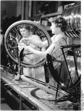 "Auf dem Fließband werden die einzelnen Teile des Rades montiert. -Bei der Montage des Vorderrades.-" (Juli 1956)