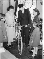 "In der HO-Fahrzeuge in der Stalinallee, Ecke Koppenstrasse interessiert sich die Familie Großkopf aus Angermünde für ein Damenfahrrad des VEB Elite-Diamant, das ihnen die Verkäuferin Ingeborg Jaschke vorführt. Das Fahrrad kostet 465.- DM." (Mai 1956)