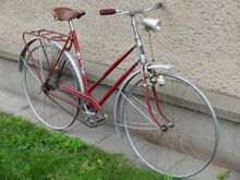 Dieses Exemplar aus der ersten Jahreshälfte 1955 besitzt bereits einen Flachlenker, hat noch Flachschulterfelgen und ist mit Blockpedalen ausgestattet. Beleuchtungskomponenten von FEK. Reifen, Klingel, Werkzeugtasche und Luftpumpe fehlen. Kleidernetz aus schwarzem Gummi vermutlich original.