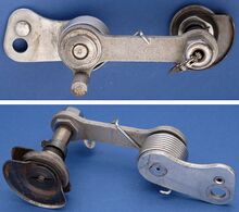 Zeitraum: 195x bis 1954 Verwendung: Zubehörteil Material: Stahl (matt verchromt/brüniert) Bemerkungen: Dreigang-Schaltwerk für die Verwendung mit starren Naben und Freilaufnaben (Rücktritt); kurze Kettenleitbleche; weiterproduziert von Optima