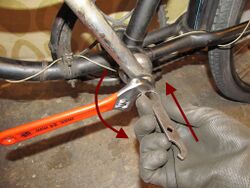 2. Entfernen der Sicherungsmutter Der erste Arbeitsgang am Tretlager ist das Lösen der Sicherungsmutter (Schlitzmutter). Stehen hier- für keine Spezialwerkzeuge zur Verfügung kann auch ein sogenannter Torpedo-Schlüssel, wie im Bild gezeigt, zweckentfremdet werden. Die Maul- schlüsselseite wird hierfür mit einer Hand kräftig in die Schlitzmutter gedrückt, während er mit einem Rollgabelschlüssel in der anderen Hand entgegen des Uhrzeigersinns (Rechtsgewinde) gedreht wird.