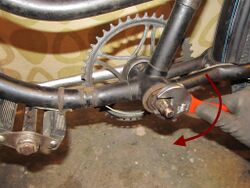 7. Lösen der Innenlagerteile Um an die Kugellager des Tretlagers zu kommen, muss zunächst die Sicherungsmutter (flache Sechskantmutter) auf der Tretlagerwelle gelöst werden. Um diese Arbeit zu erleichtern, bietet es sich an, eine alte Pedale von innen in die rechte Kurbel zu schrauben, sodass sich diese am Rahmen abstützt. Achtung: Die Sicherungsmutter besitzt ein Linksgewinde und muss zum Lösen im Uhrzeigersinn gedreht werden! Nun kann die flache Nasenscheibe abgezogen werden und der Konus gelöst werden.